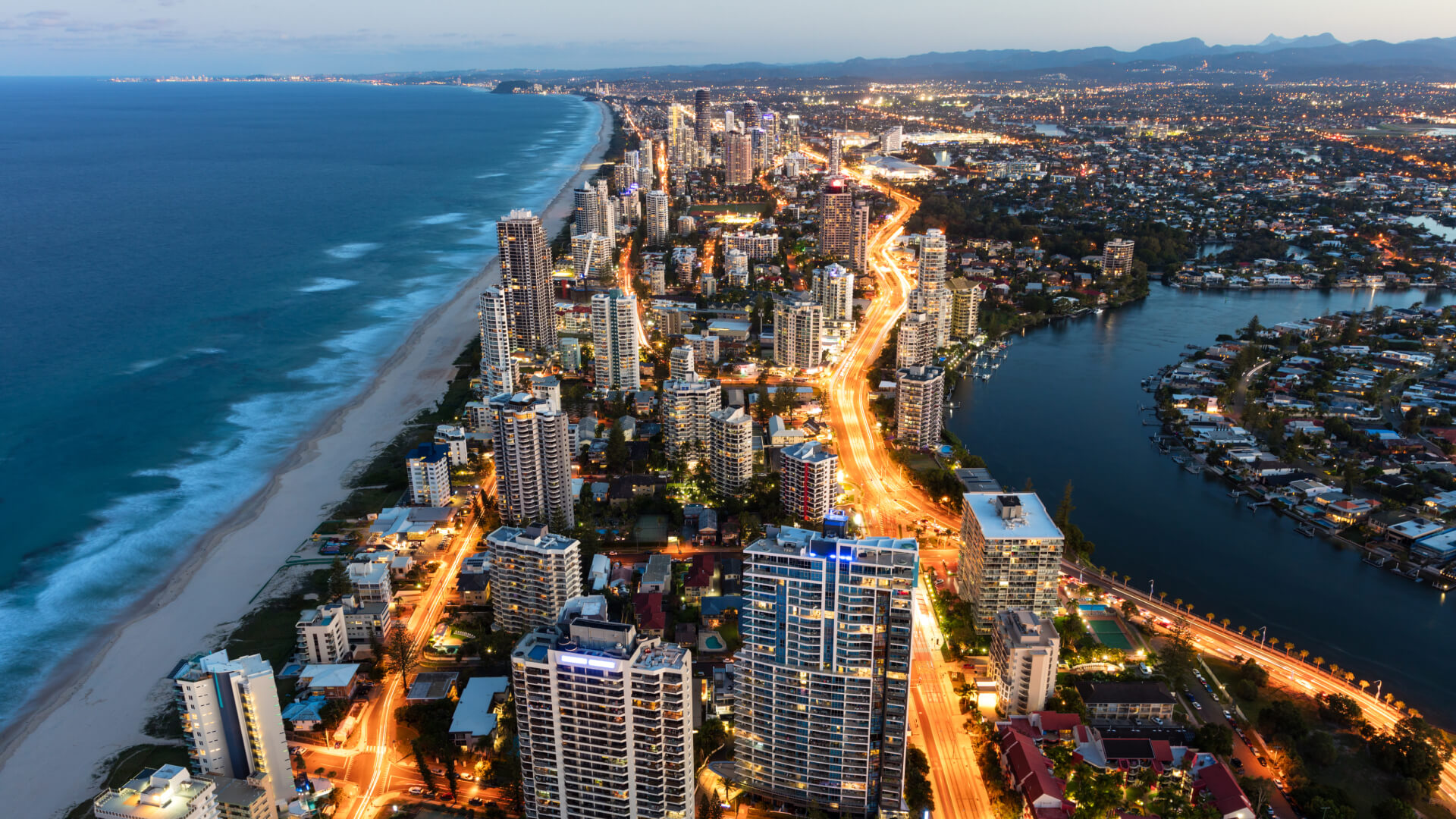 Aerial view of the Gold Coast skyline at dusk with illuminated city streets running alongside the beach.