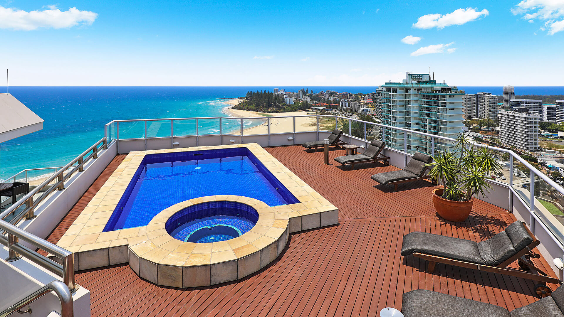 Rooftop pool and spa deck of the 4 Bedroom Oceanfront Penthouse at ULTIQA Points North Coolangatta, featuring sun loungers, timber decking, and sweeping ocean and coastline views.