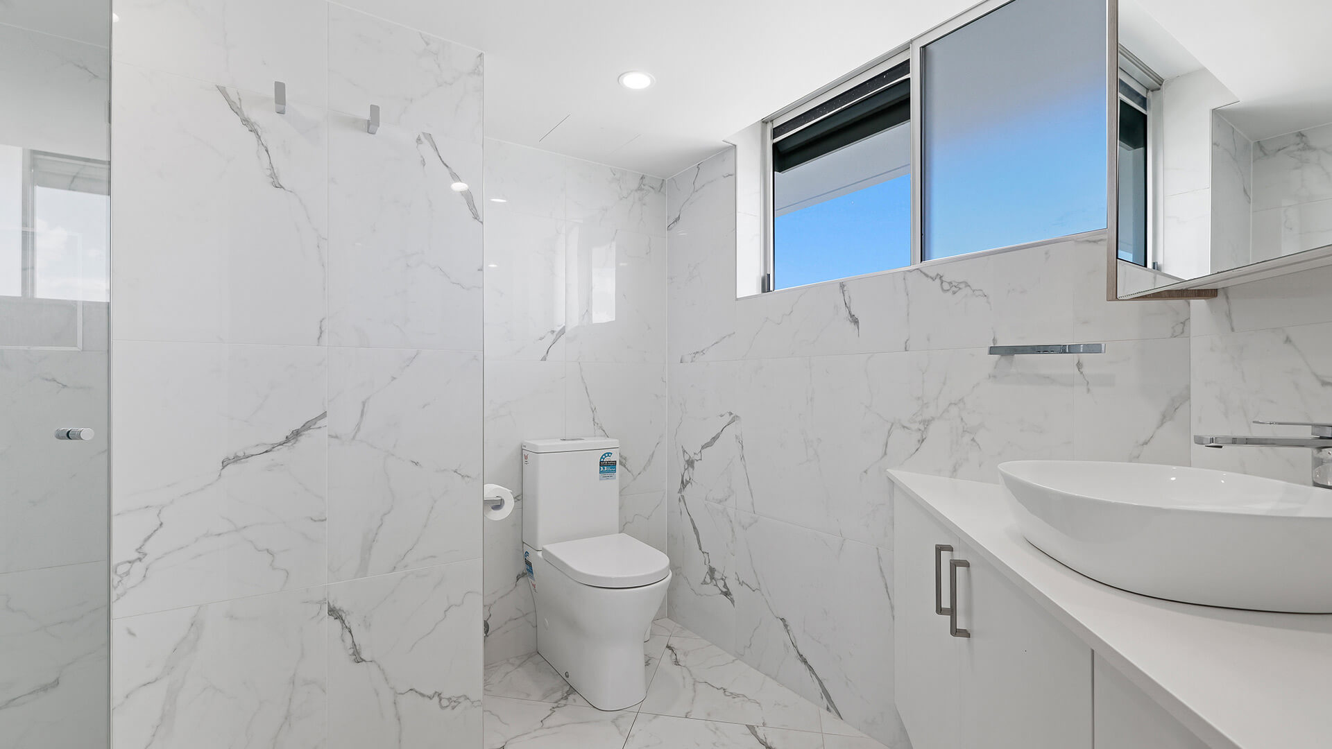 Modern bathroom in the Deluxe 3 Bedroom Ocean View Apartment, featuring marble-look tiles, a walk-in shower, toilet, and vanity with a vessel basin.