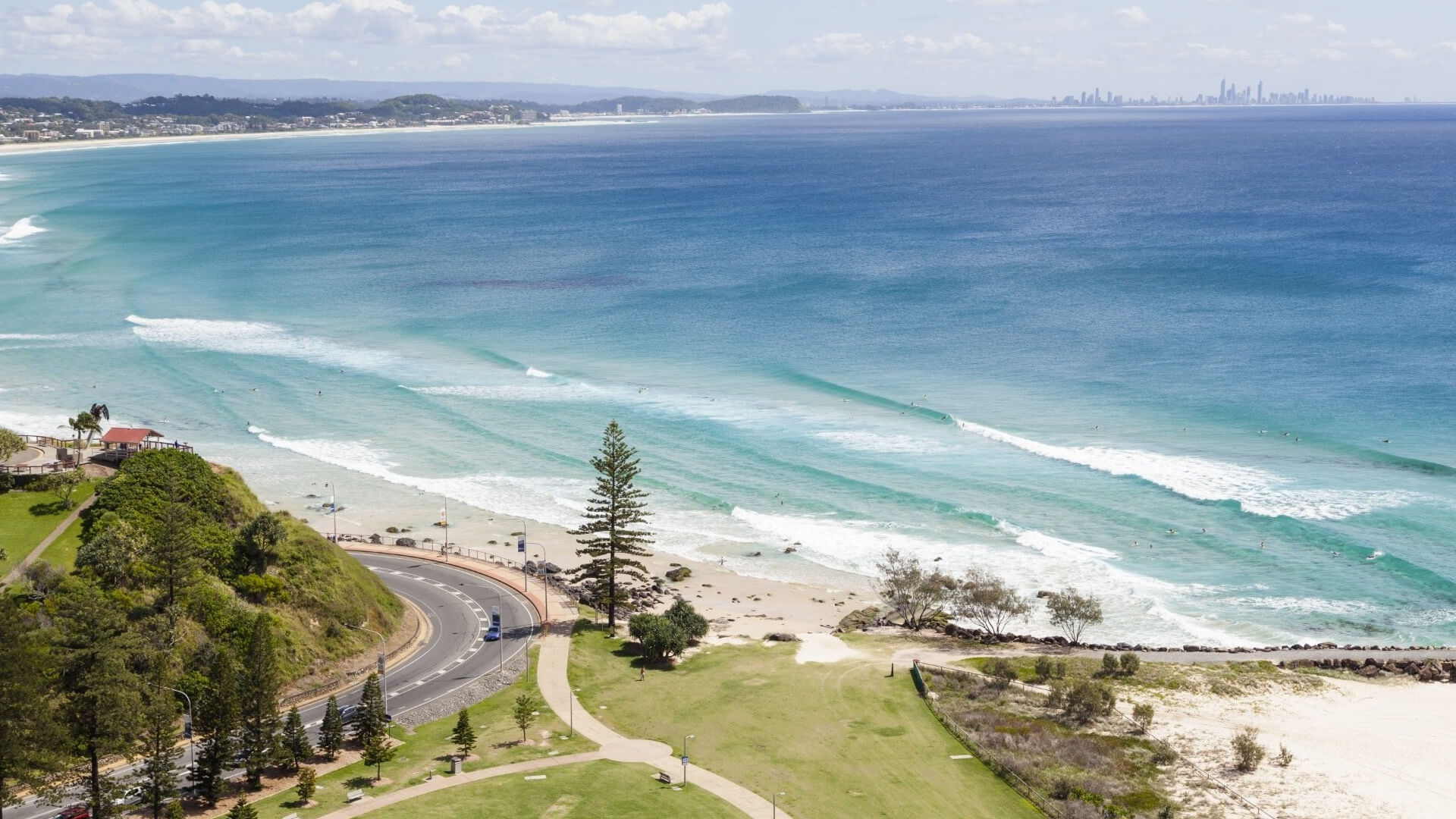 Aerial view from Coolangatta overlooking turquoise waves and the Gold Coast skyline in the distance.