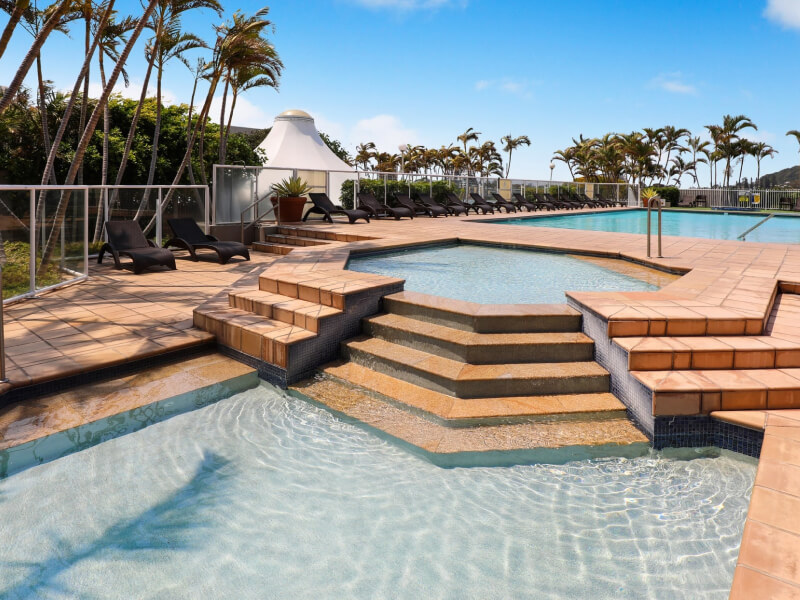 Resort pool area at ULTIQA Points North with sun loungers, palm trees, and a large swimming pool under a clear blue sky.