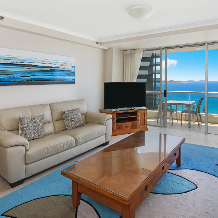 Spacious apartment living room at ULTIQA Points North featuring ocean views, comfortable leather sofas, a flat-screen TV, and a private balcony overlooking the beach.