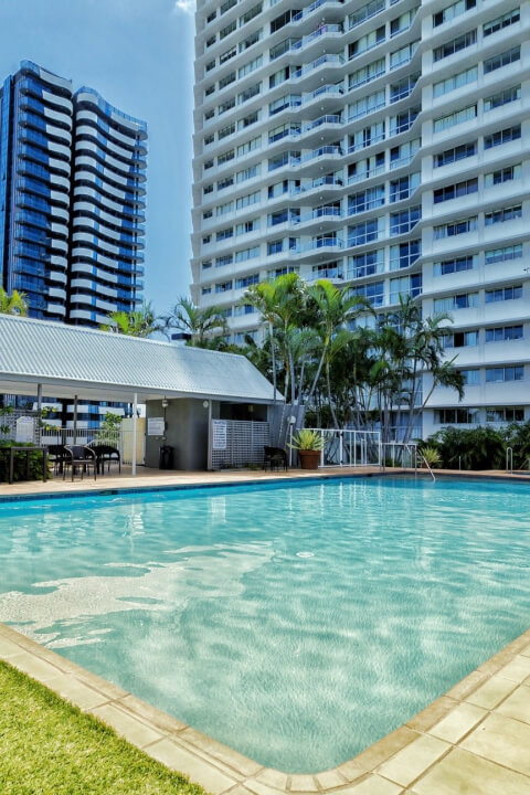 Outdoor pool area at ULTIQA Points North featuring sun loungers, tropical palm trees, and views of the resort's high-rise building.