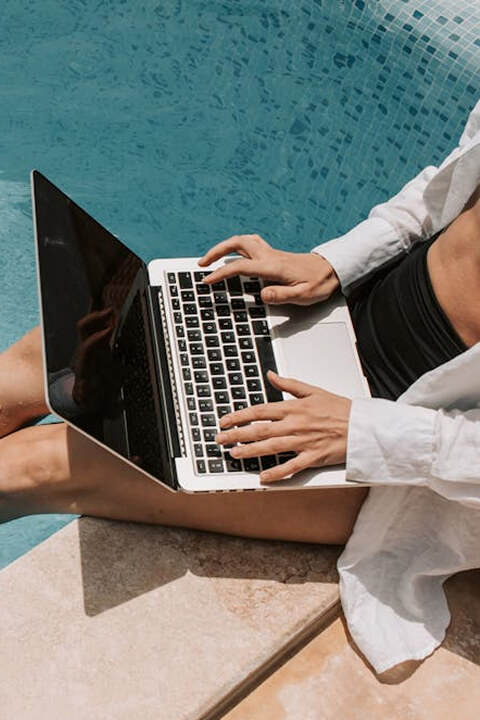 Person working on a laptop beside a pool, enjoying a relaxed and sunny setting.