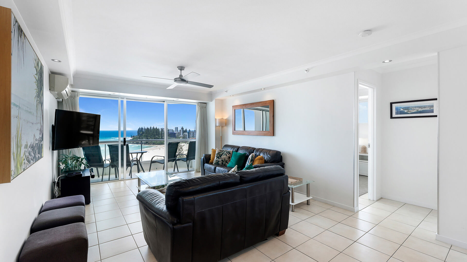Living area in the 2 Bedroom Superior Ocean View Apartment with leather sofas, tiled floors & balcony access showcasing expansive ocean & beach views.
