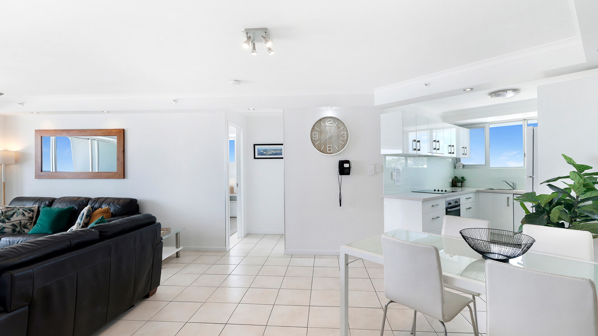 Open-plan living & dining area in the 2 Bedroom Superior Ocean View Apartment with tiled floors, white dining set, leather sofa & modern kitchen with ocean views.