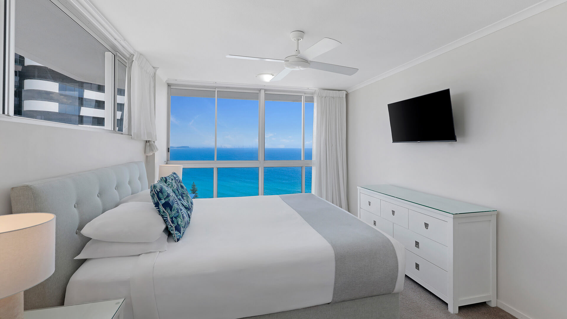 Master bedroom in the Superior 3 Bedroom Ocean View Apartment featuring queen bed, soft coastal décor & sweeping ocean views through large windows.