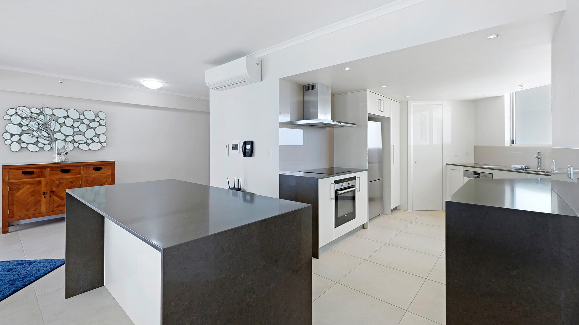 Modern kitchen in the Superior 3 Bedroom Ocean View Apartment featuring stone benchtops, stainless-steel appliances, and ample storage.