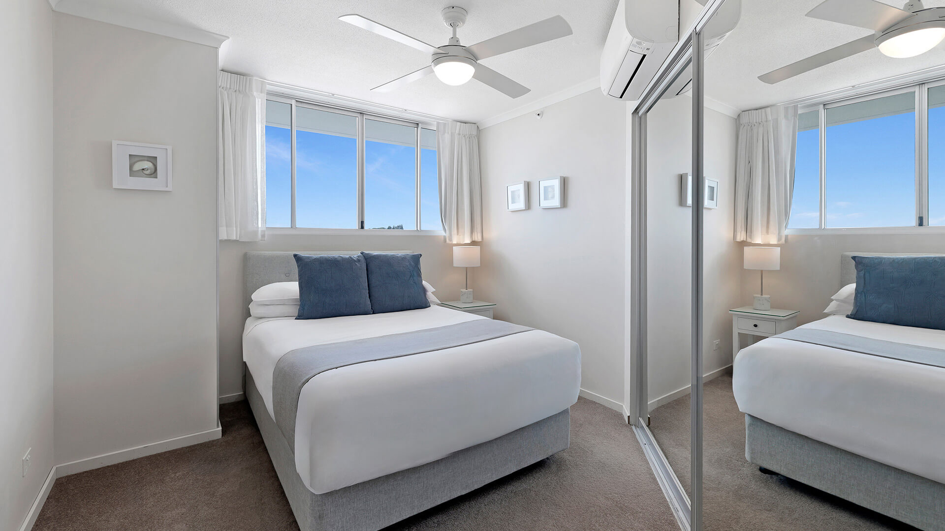 Bright secondary bedroom in the Superior 3 Bedroom Ocean View Apartment featuring a queen bed, mirrored wardrobe, ceiling fan, and soft coastal décor.