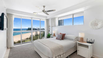 Master bedroom in a 2 Bedroom Superior Ocean View Apartment featuring queen bed, soft neutral décor, large windows with sweeping ocean & beach views.