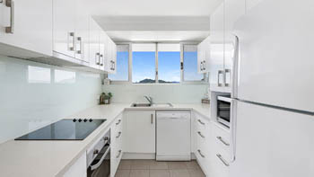 Modern kitchen in a 2 Bedroom Superior Ocean View Apartment featuring white cabinetry, stainless-steel appliances and ocean & hillside views.