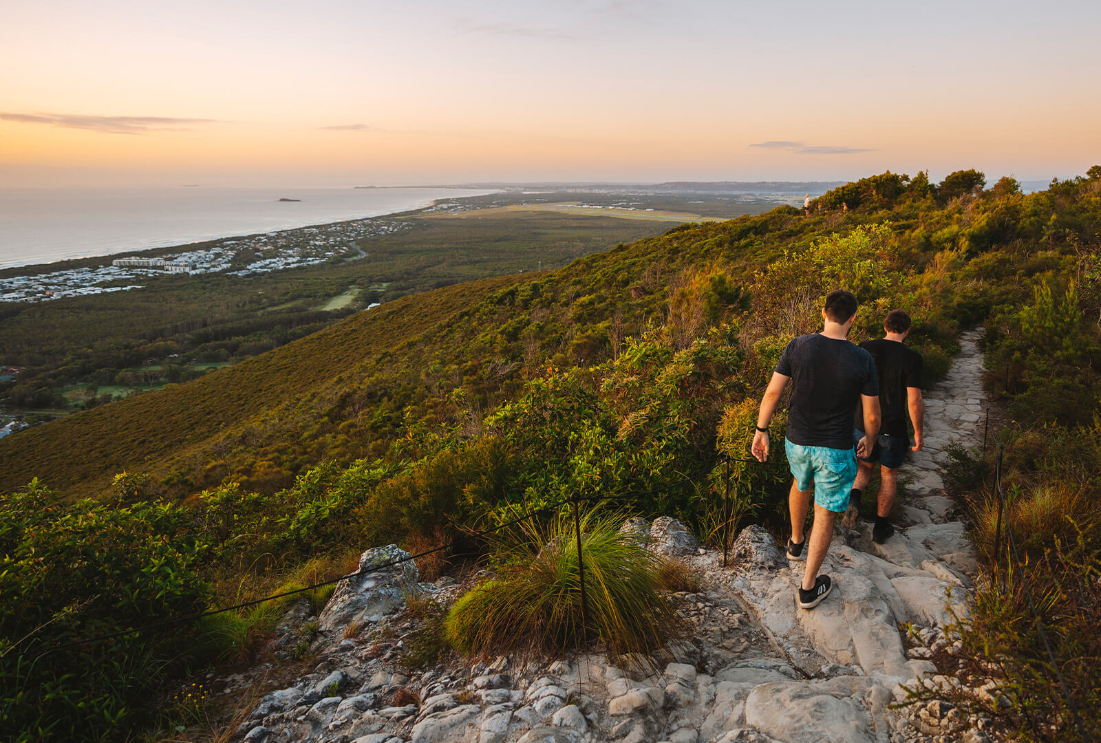 Aerial view of Tallebudgera Creek at Burleigh Head National Park, with turquoise water, sandy beach, and paddleboarders near the forested shoreline