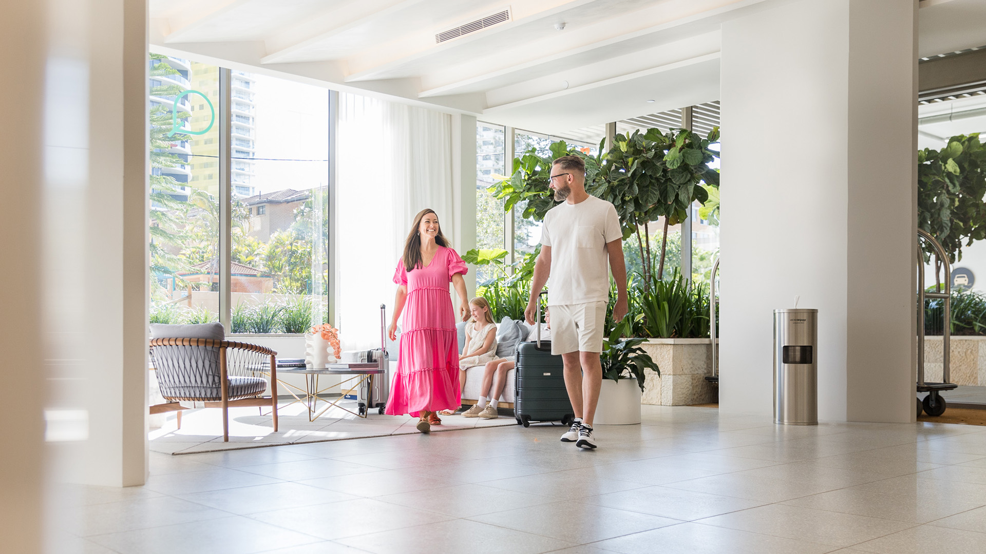 Family walking through the bright, modern lobby of ULTIQA Signature at Broadbeach, with large windows, indoor plants, and contemporary seating.