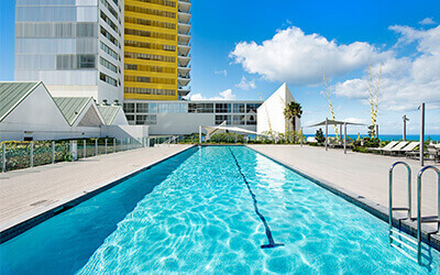 Outdoor swimming pool at ULTIQA Air on Broadbeach with sun loungers, deck area, and ocean views in the background.