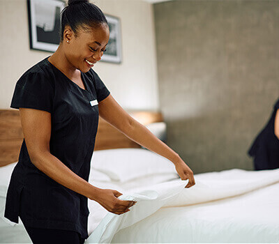 Smiling housekeeping staff making a neatly dressed bed in a hotel room.